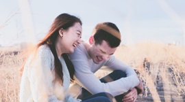  A photo of an Asian woman and Western man heartily laughing while sitting next to each other in a grass field